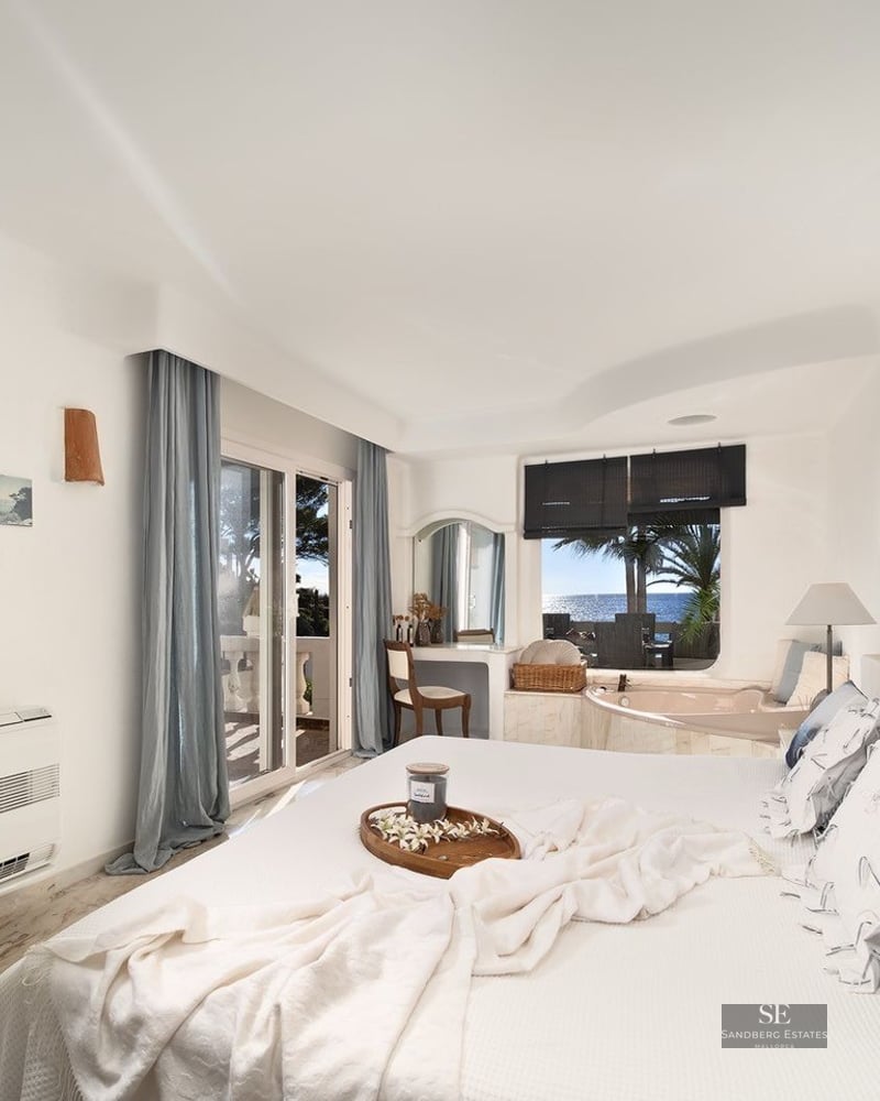 Bright white master bedroom featuring a built-in bathtub by the window and a balcony overlooking the sea.