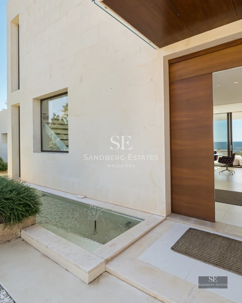 Exterior view of a modern house with a pool, large windows, wooden terrace, and lush vegetation. Minimalist architecture.