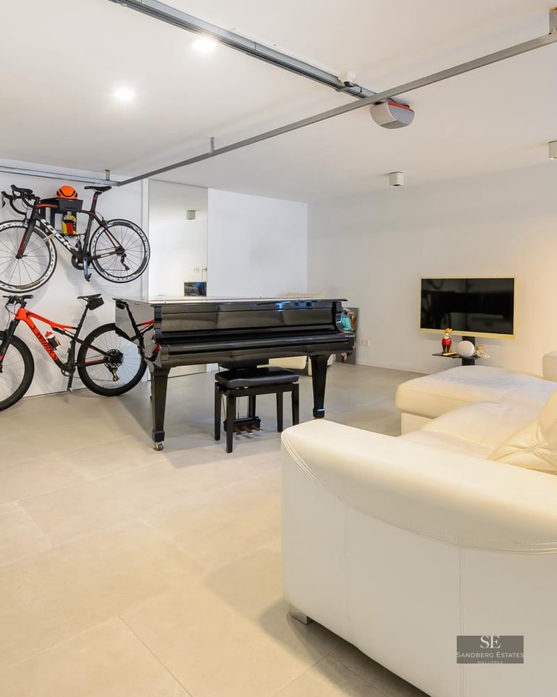 Modern white room featuring a black grand piano, wall-mounted bicycles, and a white leather sofa on grey tiled floors.
