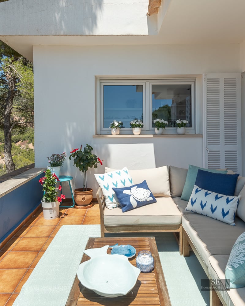 Outdoor terrace with a large L-shaped sofa, blue cushions, and a wooden table overlooking a pine forest valley.
