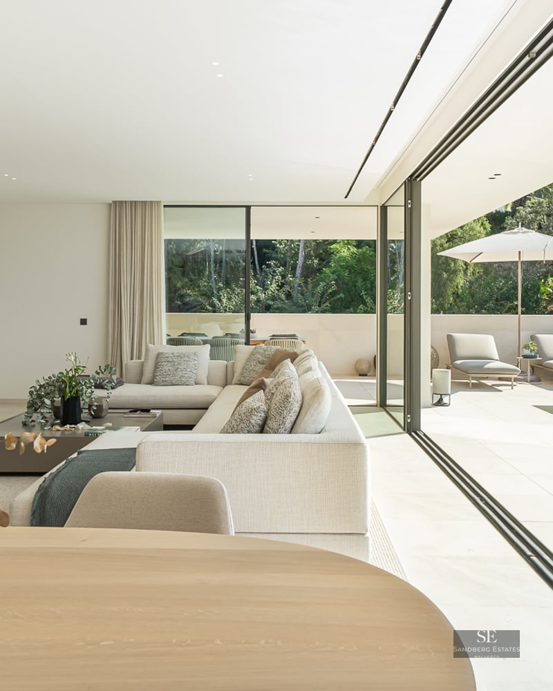 Modern bright living room with large glass doors opening to a sunlit terrace and private swimming pool.