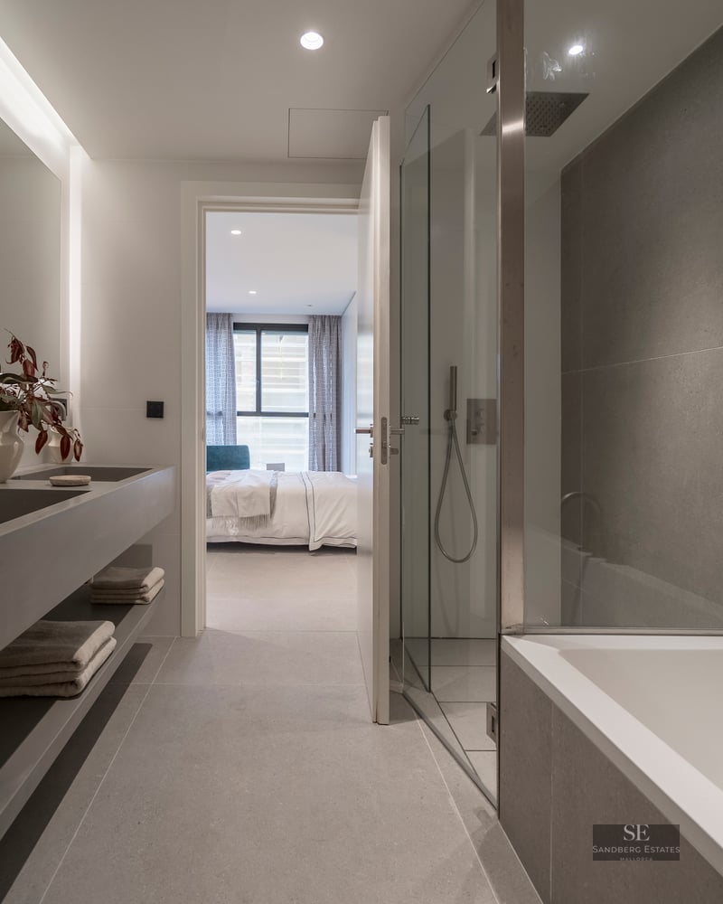 Contemporary bathroom featuring a gray floating double sink, glass shower, bathtub, and a view into the bedroom.
