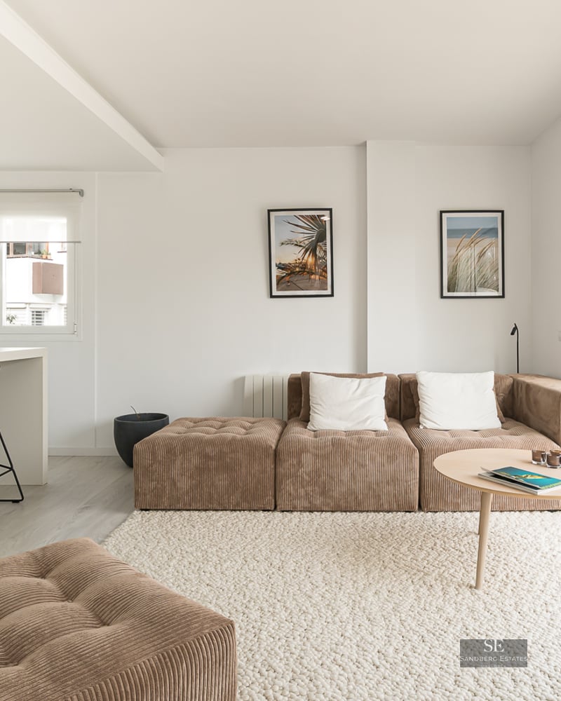 Bright living room with brown corduroy modular sofa, white textured rug, kitchen island, and large glass doors to a balcony.