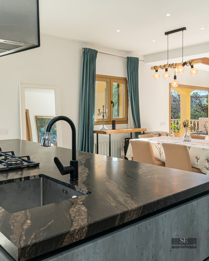 Modern kitchen island with dark stone countertop opening into a dining and living area with a fireplace.