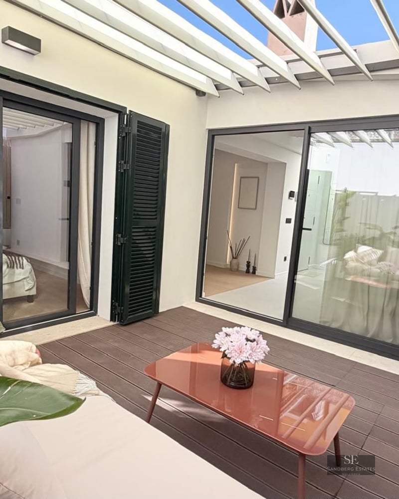 Outdoor patio with white pergola, wooden deck, terracotta-colored furniture, and tropical plants.