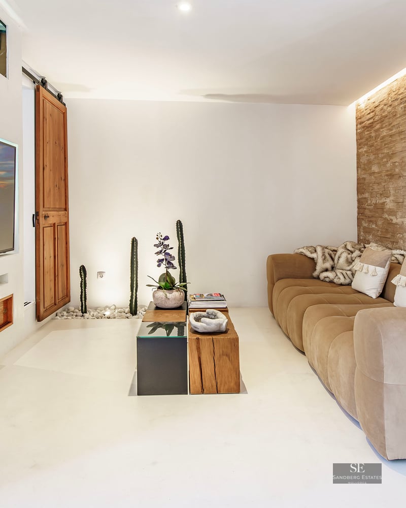 Living room featuring a beige sofa, rustic stone wall, built-in television, and Mediterranean decor elements.