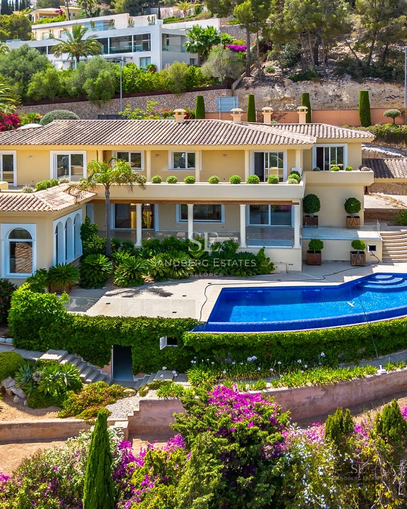 View of a luxury infinity pool with sun loungers and umbrellas, surrounded by a garden and overlooking the sea. Modern and elegant architecture.