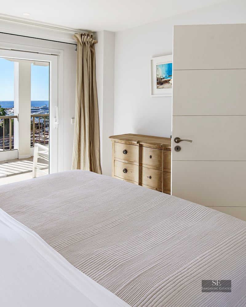 Bright bedroom featuring a large bed, sliding doors to a terrace, and panoramic views of a marina.