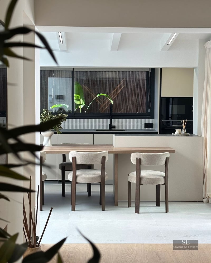 Modern kitchen featuring a light wood dining table attached to a beige island, with stylish chairs and a large window.