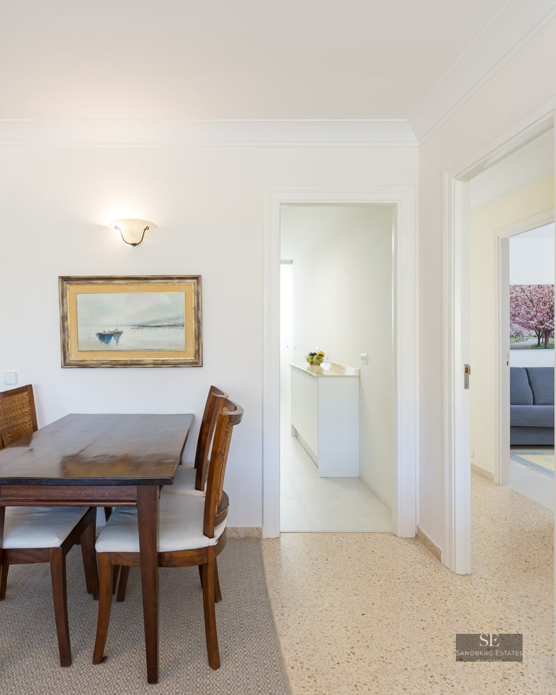A dark wood dining table and four chairs with woven backs and white cushions in a bright, white room.