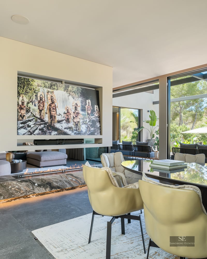 A luxurious open-plan living room with a linear marble fireplace, modern seating, and floor-to-ceiling glass garden doors.