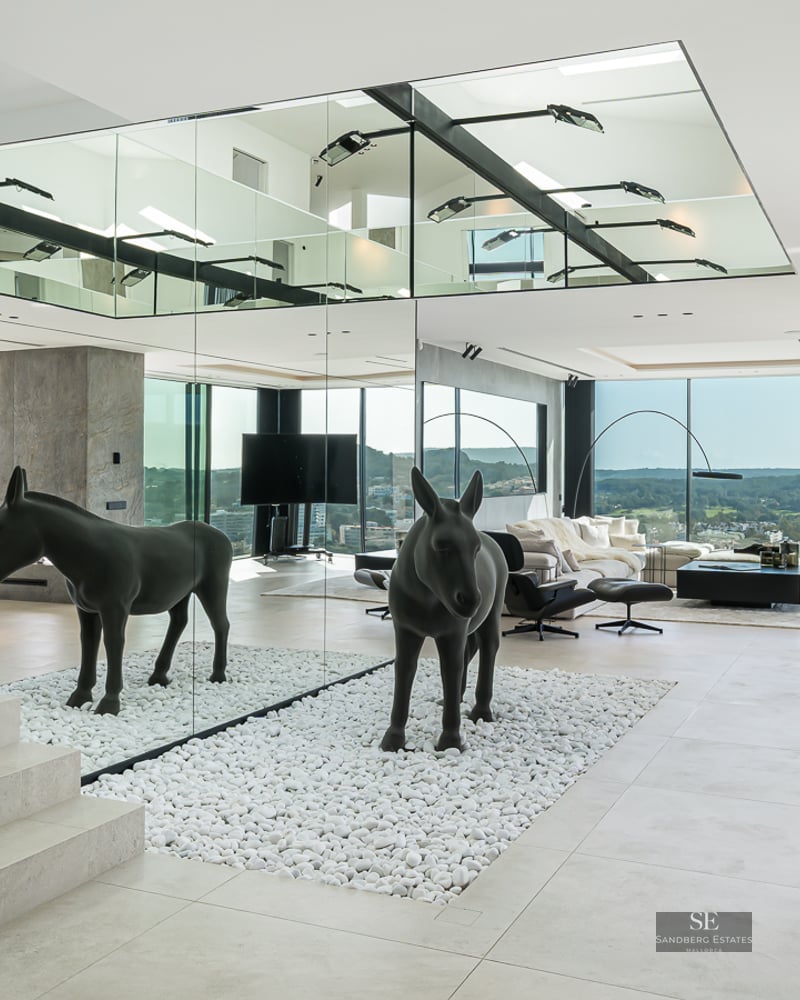 Modern living room featuring a mirrored wall, black donkey sculpture on white pebbles, stone stairs and views.