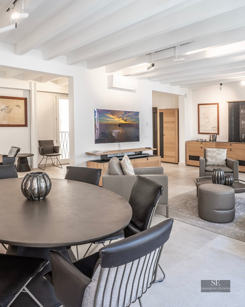 Salon moderne avec table ronde, canapés en cuir, plafond à poutres blanches et télévision murale.