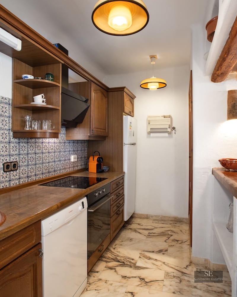 Narrow kitchen featuring dark wood cabinets, marble flooring, exposed beams, and traditional patterned tiling.