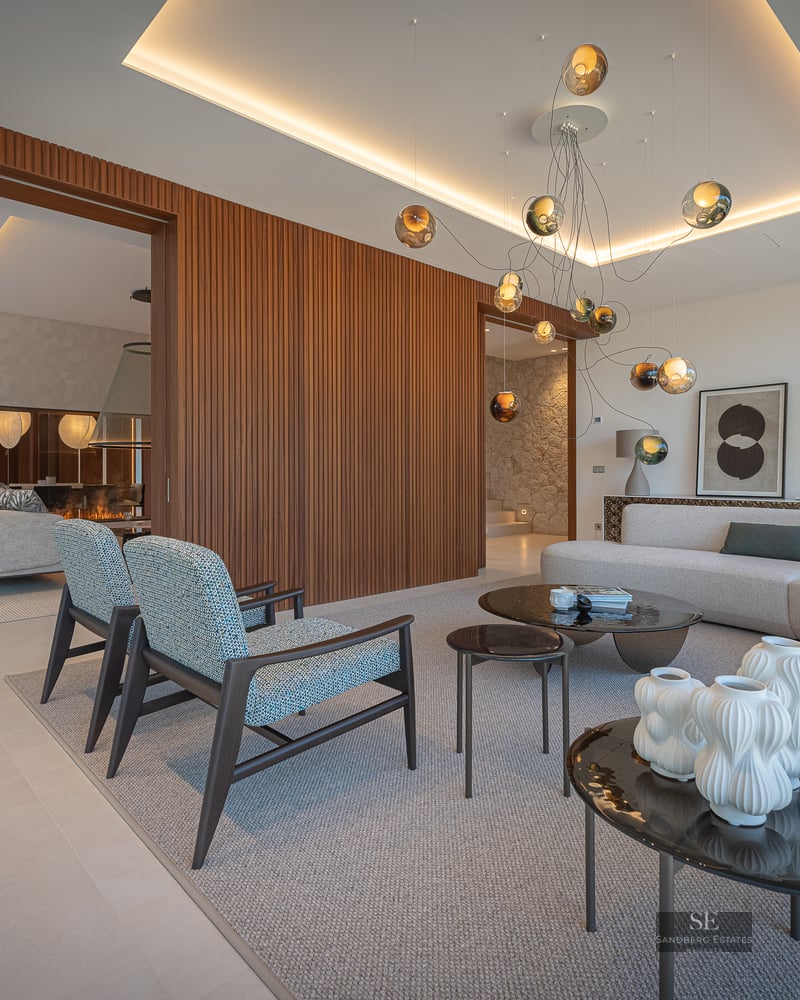Modern living room with a large gray sofa, blue armchairs, wood slatted wall, and a unique glass orb chandelier.