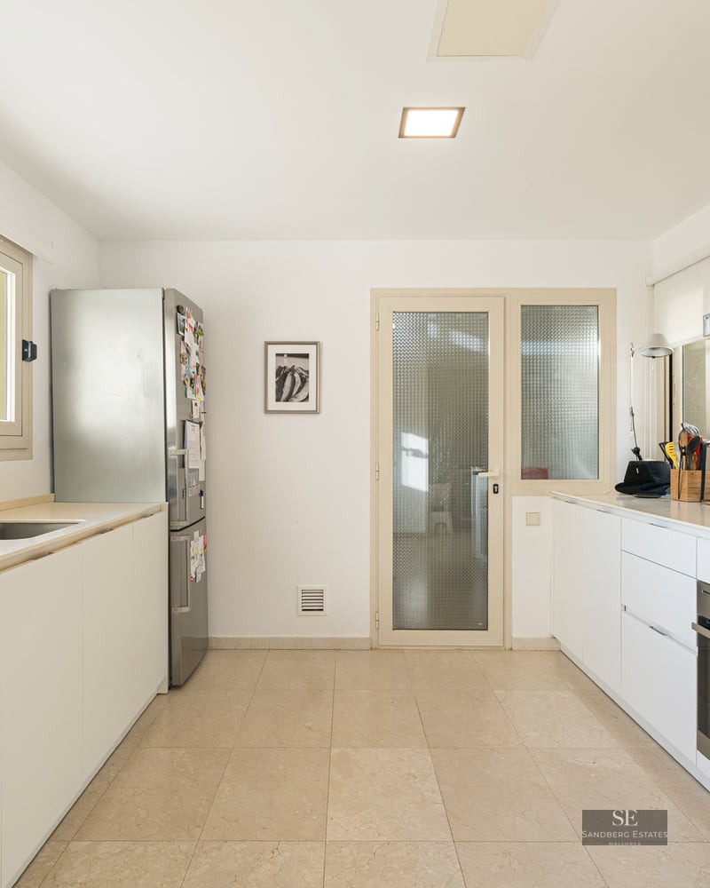 Bright kitchen with white cabinets, stainless steel fridge and oven, and a large window overlooking green trees.