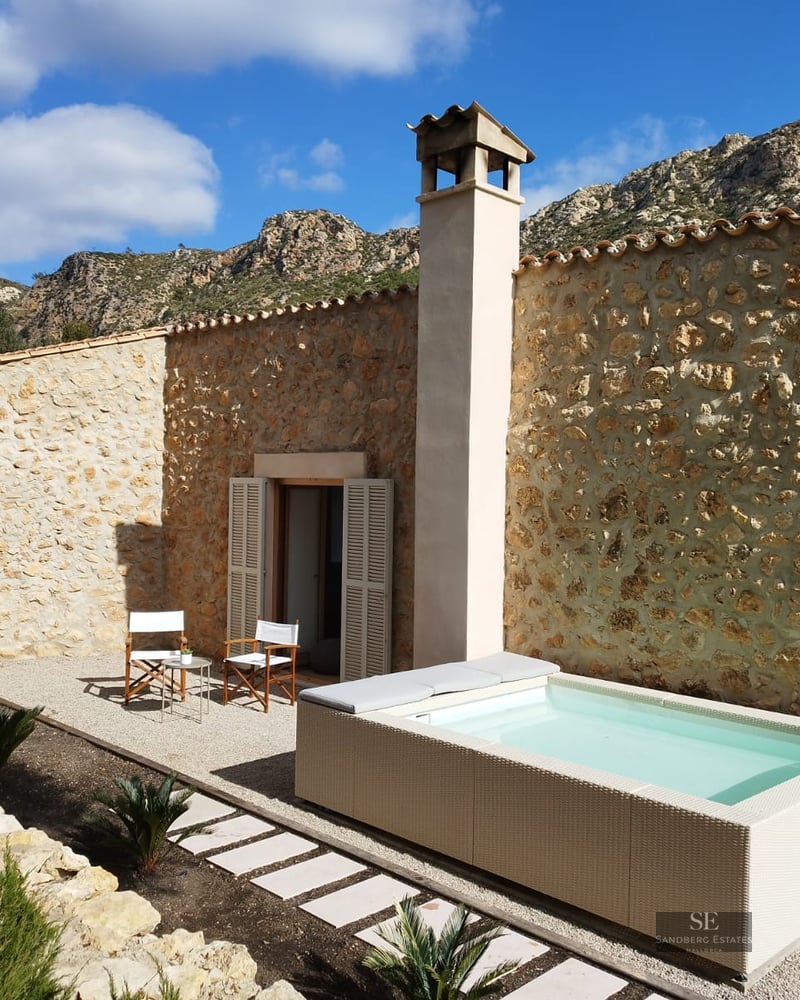 Small rectangular plunge pool on a gravel terrace next to a stone house with mountain views.
