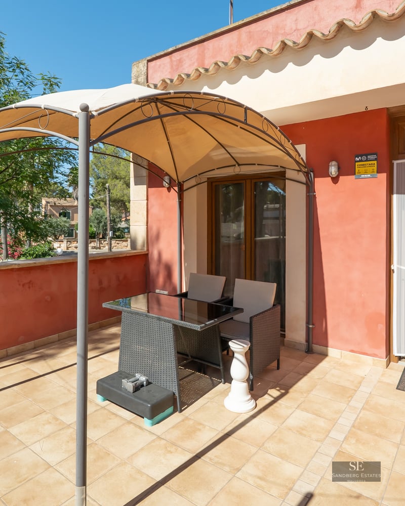 Sunny terrace with terracotta walls, a tiled floor, and a metal gazebo over a table and two chairs.