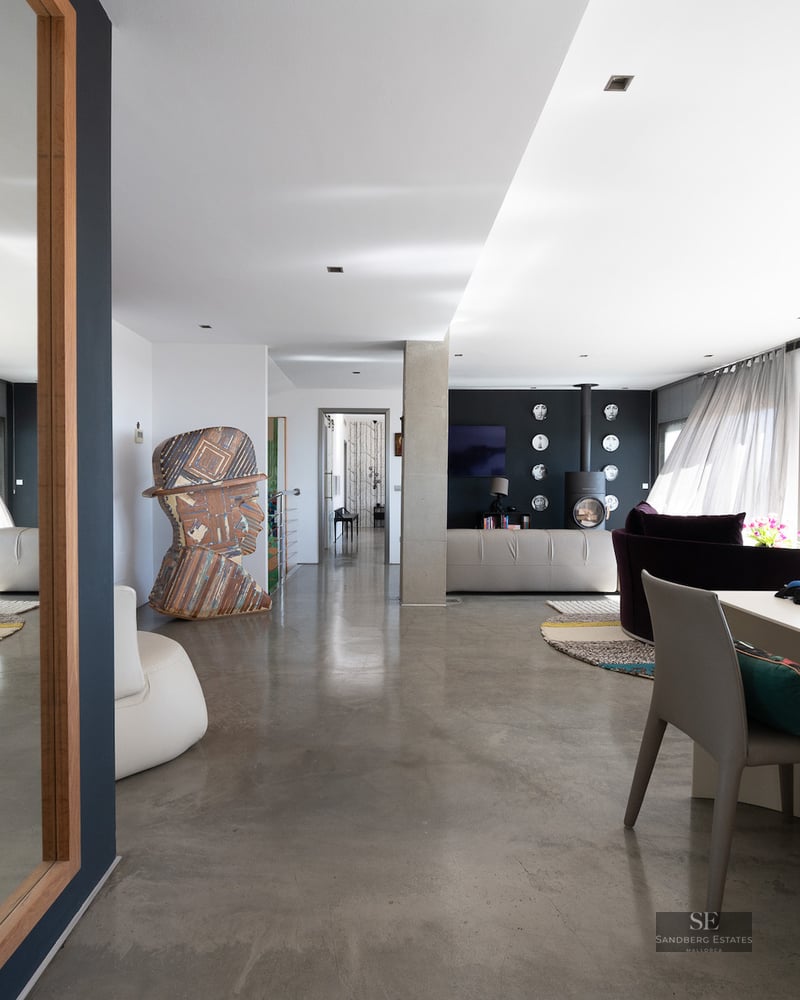 Bright interior with polished concrete floors, a large mirror reflecting a sofa, and contemporary art sculptures.