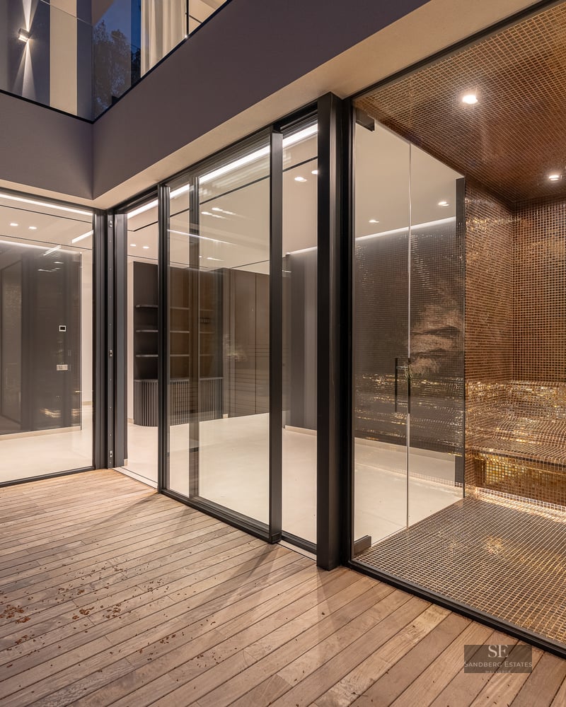 Modern spa area featuring a wooden sauna and gold mosaic steam room behind glass walls and a wooden deck.