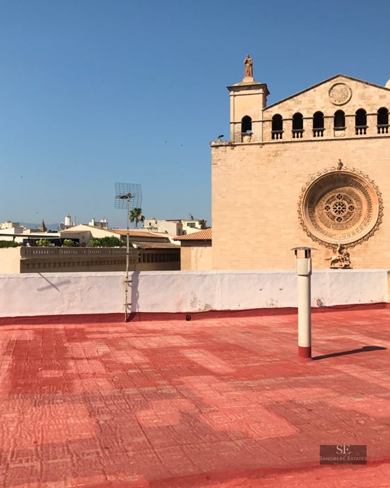 Red tiled rooftop overlooking a stone church facade with a rose window under a clear blue sky.