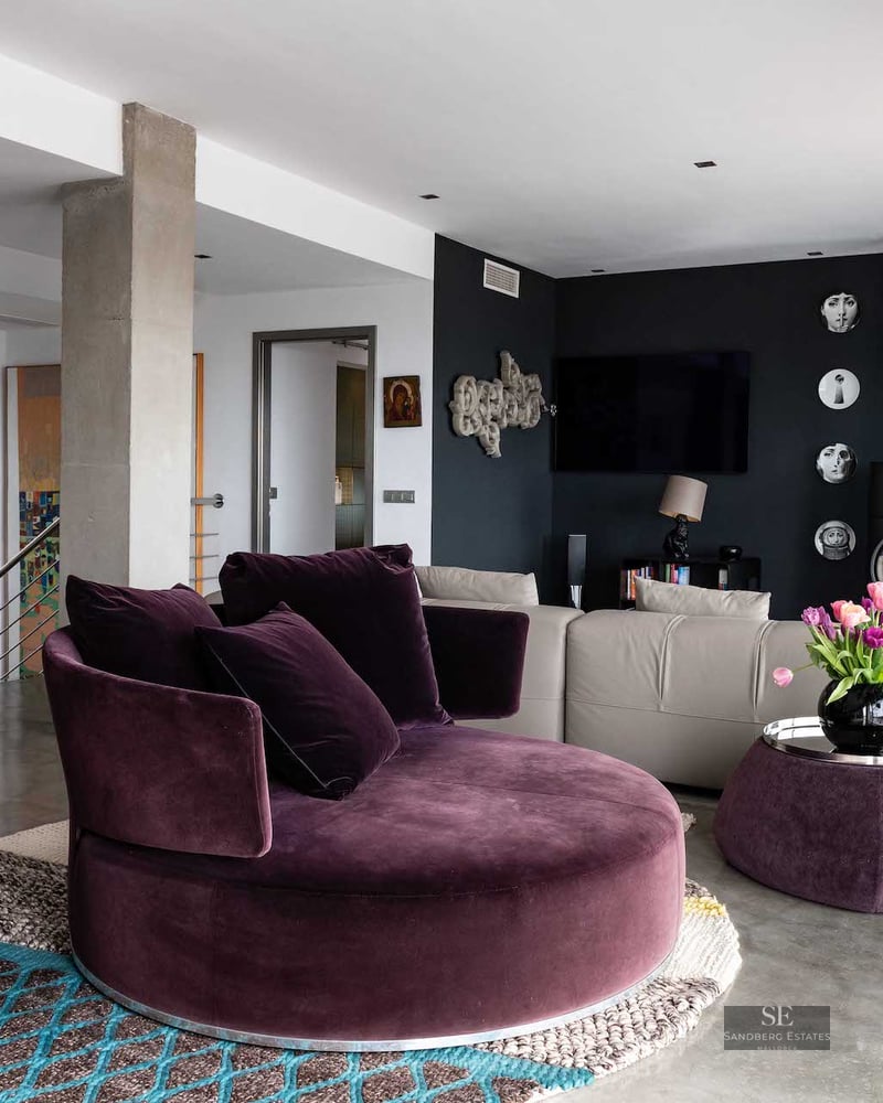 Modern living room with plum velvet circular sofa, polished concrete floors, and a black accent wall with a wood stove.