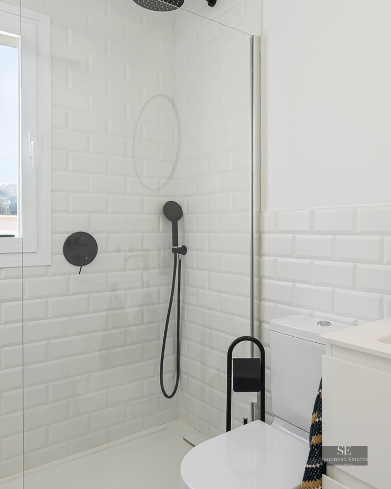 Bright bathroom featuring white subway tiles, a glass shower partition, and modern matte black fixtures.