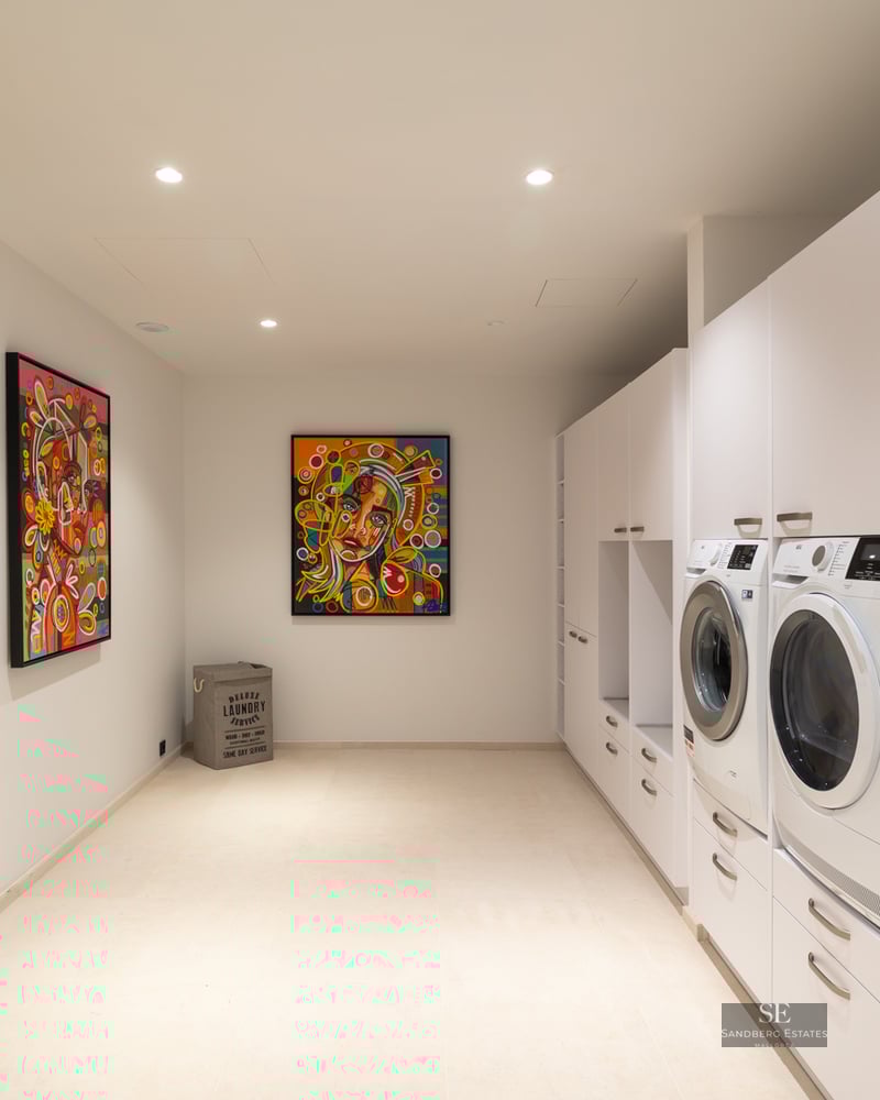 Modern white laundry room with washer, dryer, minimalist cabinetry, and three vibrant colorful pop-art portraits.
