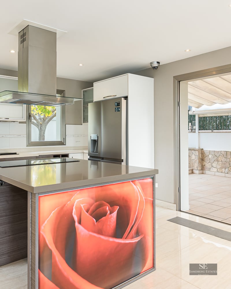 Modern kitchen featuring a large island with a red rose graphic, stainless steel appliances, and patio doors.