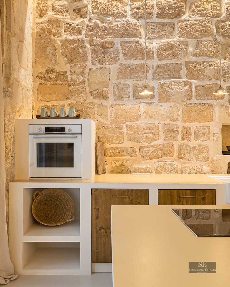 Cuisine moderne avec un grand mur en pierre apparente, des armoires blanches, des accents en bois et des appareils intégrés.