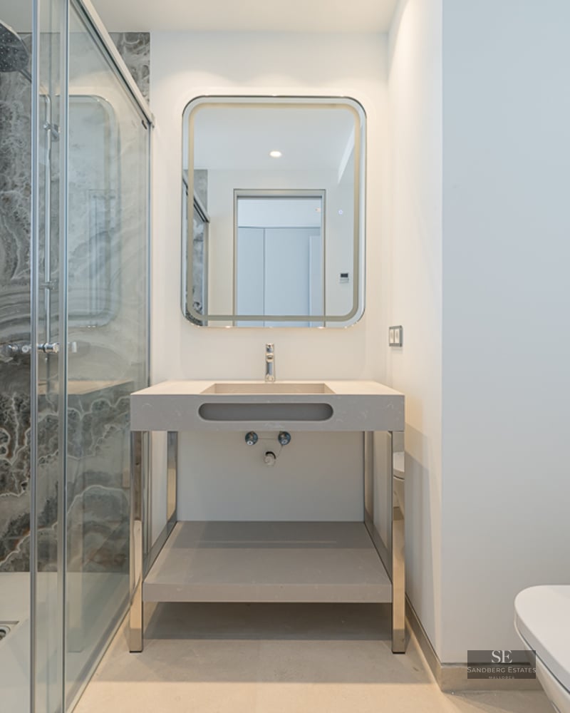 Modern bathroom with a glass walk-in shower featuring marble-patterned walls, a backlit mirror, and a minimalist sink.
