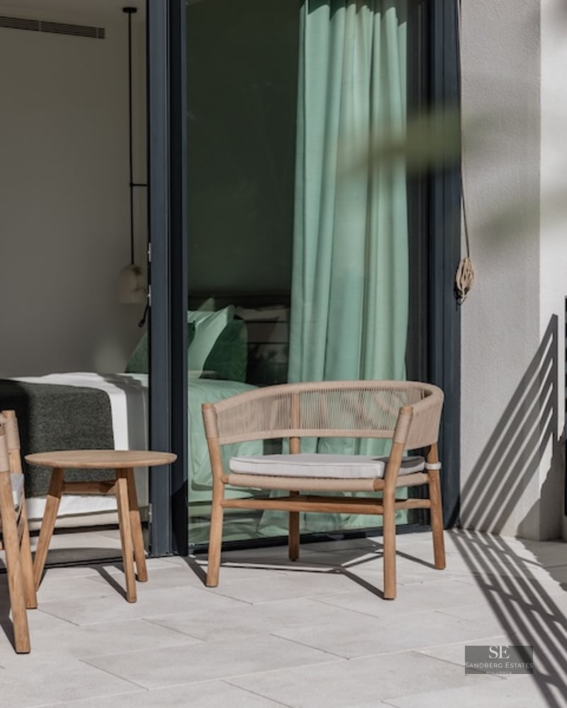 Modern terrace with woven armchairs and a small wooden table, adjacent to a bedroom with large glass sliding doors.