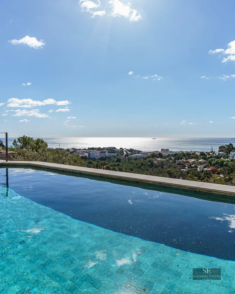 Infinity edge swimming pool overlooking a coastal town and the Mediterranean Sea under a bright sunny sky.