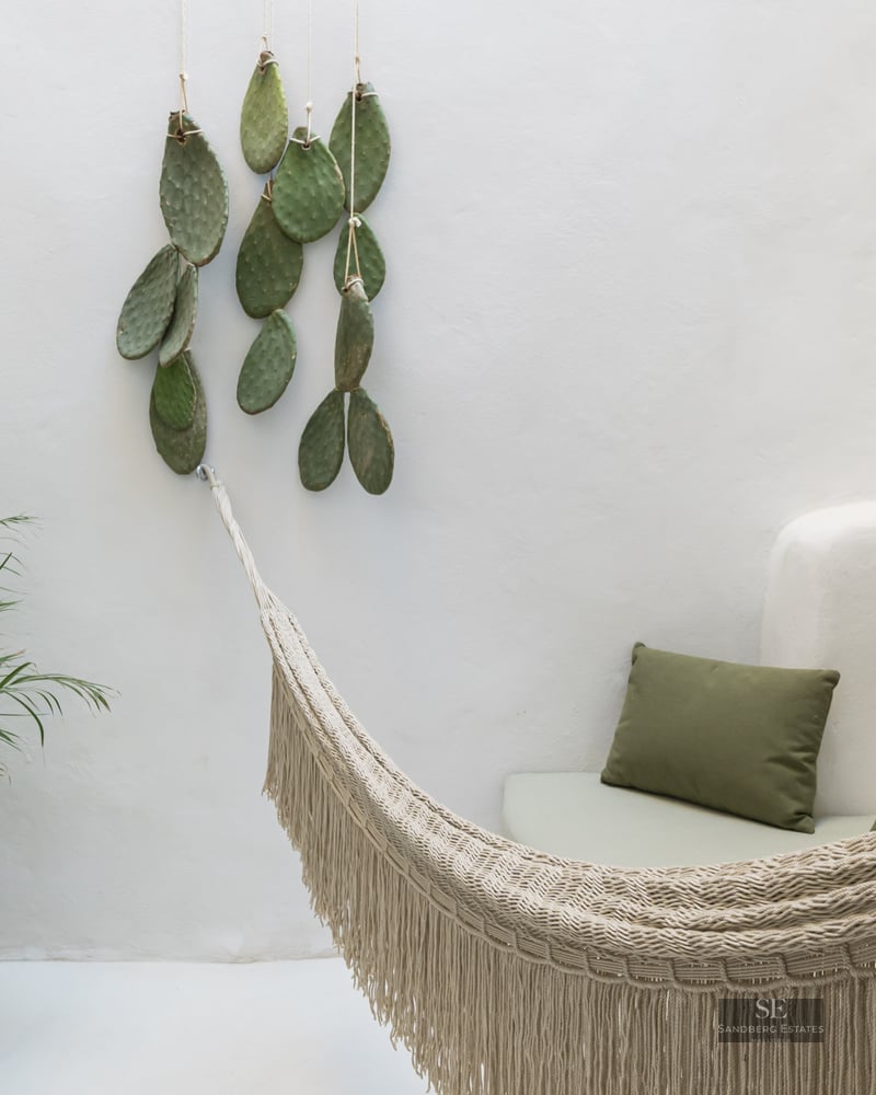 White minimalist terrace featuring a cream woven hammock, green cushions on a built-in bench, and a potted palm plant.