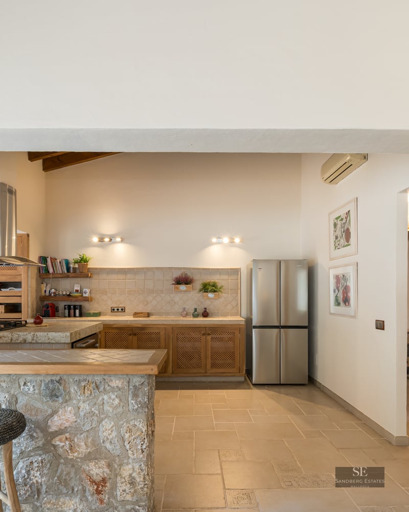 Spacious kitchen featuring a natural stone bar, stools, wooden ceiling beams, and stainless steel appliances.