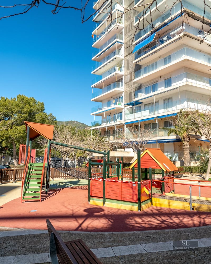 A colorful children's playground with safety flooring in front of a modern high-rise apartment building.