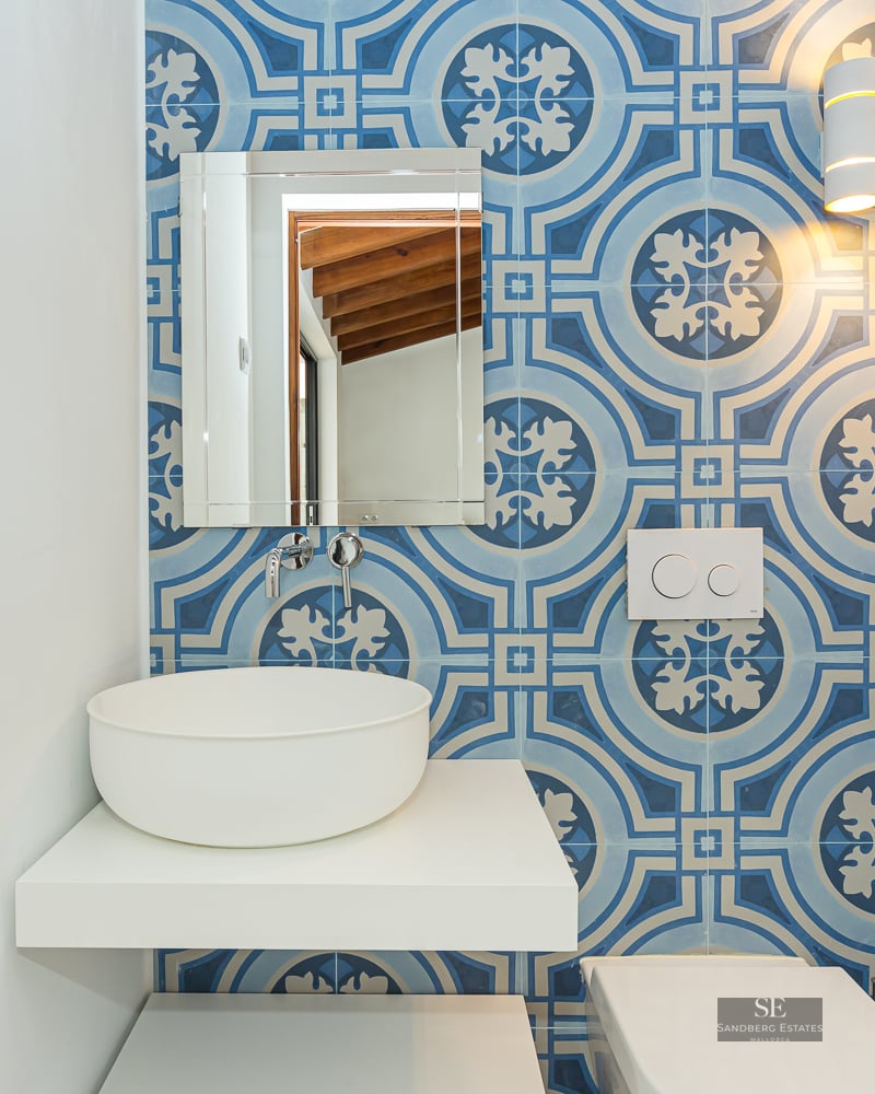 Bathroom featuring blue patterned wall tiles, a white vessel sink on a floating shelf, and a rectangular mirror.