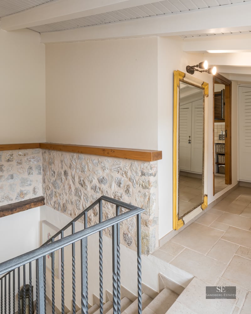 Interior landing featuring a wrought iron staircase, exposed stone walls, wooden ceiling beams, and white built-in wardrobes.