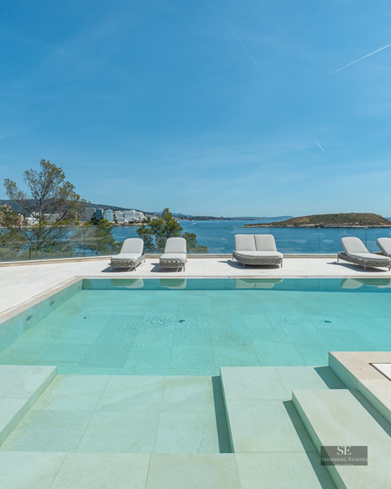 A turquoise swimming pool on a stone terrace with sun loungers overlooking the Mediterranean sea and a distant island.