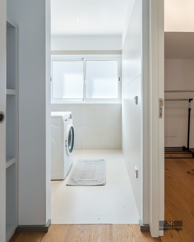 View of a white laundry room with a washing machine and an adjacent walk-in closet with wooden floors.