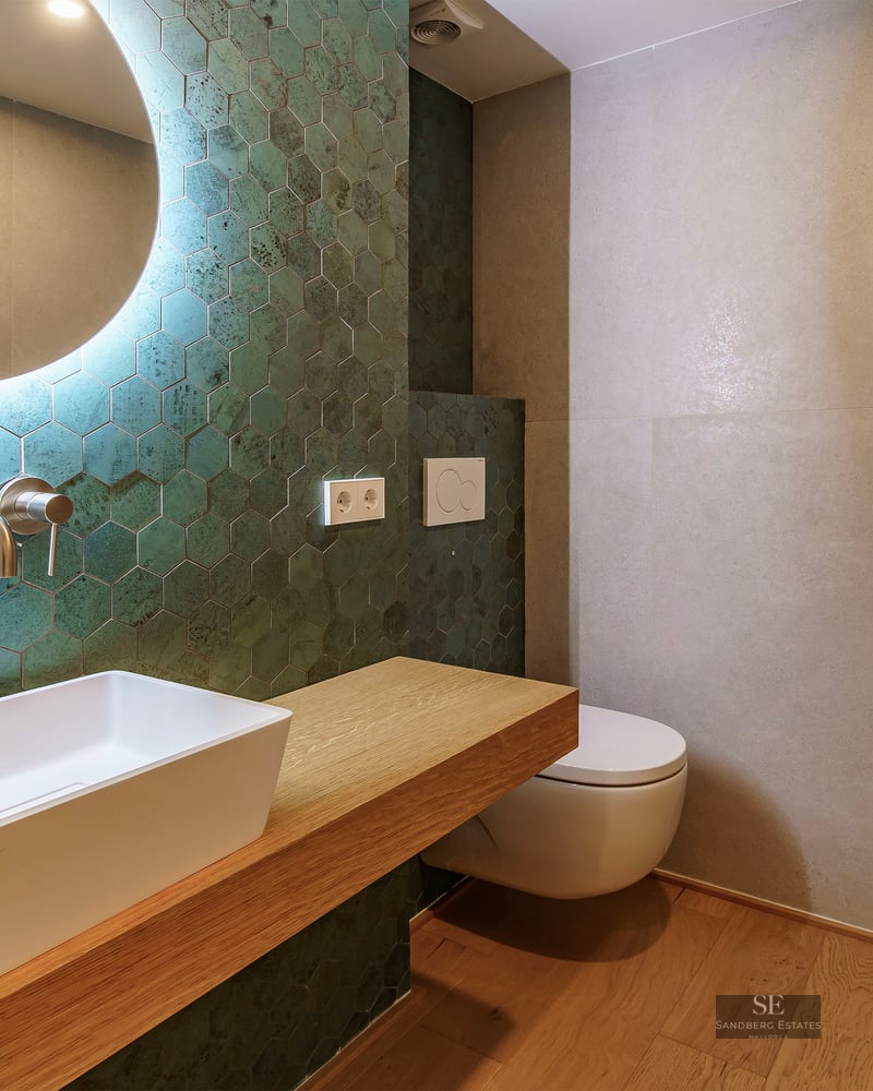 Salle de bain moderne avec carreaux hexagonaux vert canard, vasque à poser sur bois et miroir rétroéclairé.