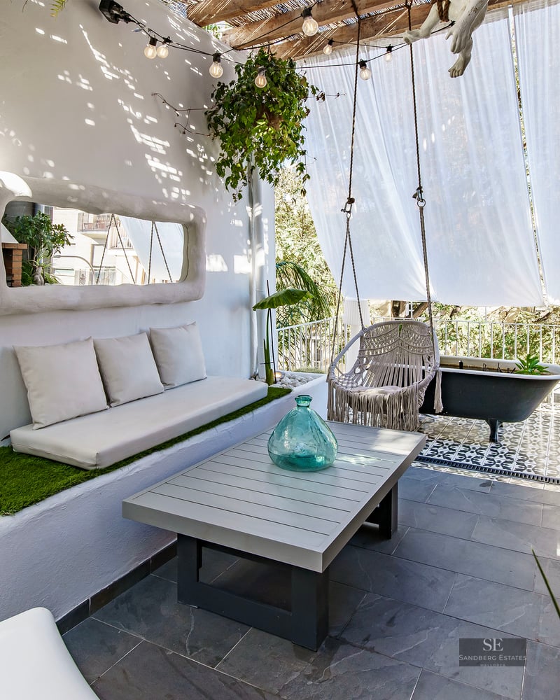 Sun-drenched white terrace with built-in sofa, macrame swing, brick outdoor sink, and a black clawfoot bathtub.