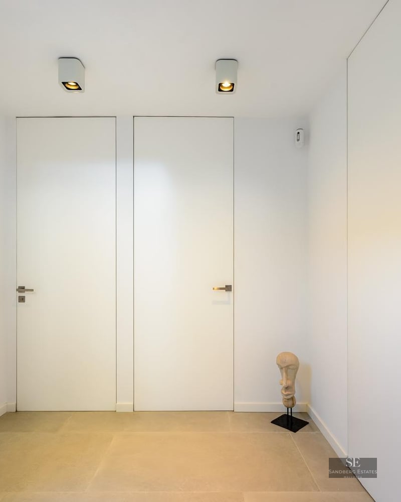 Minimalist hallway with flush white doors, light stone flooring, and a small decorative head sculpture.