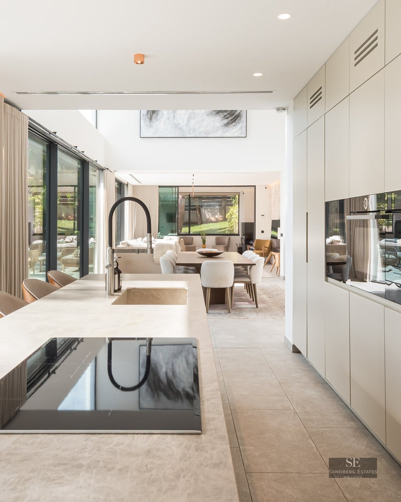 Cuisine moderne avec un grand îlot en pierre, des appareils intégrés et des baies vitrées donnant sur une piscine.