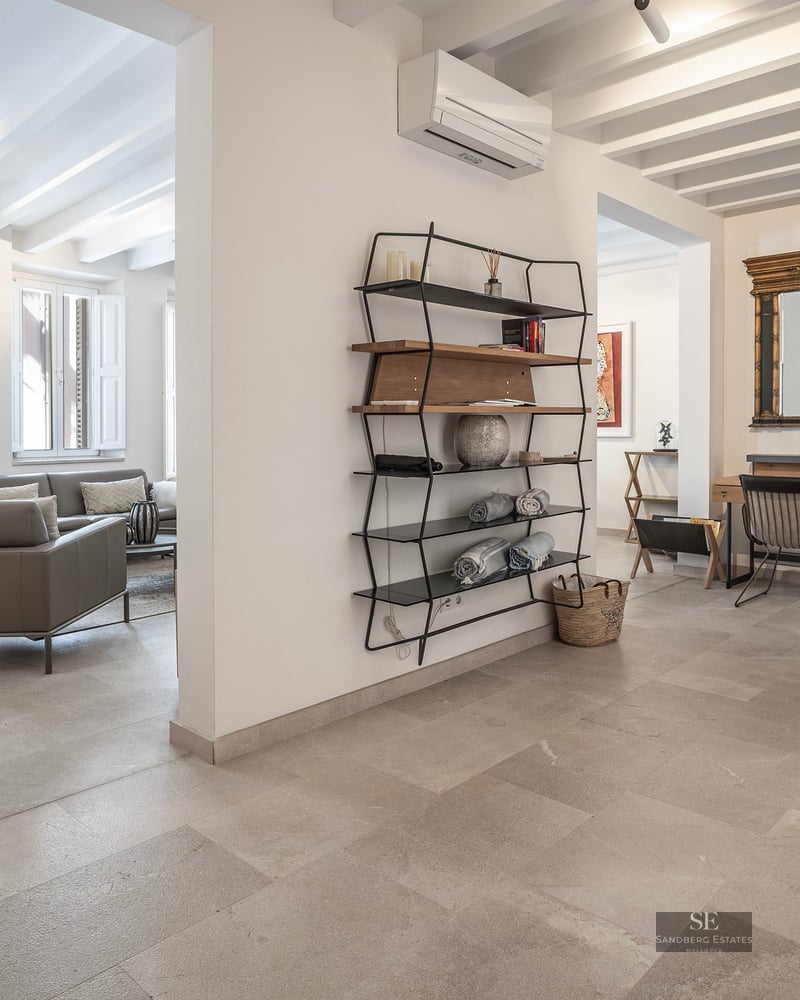 Modern interior with stone floors, white beams, grey sofa, and a study nook with a gold-framed mirror.