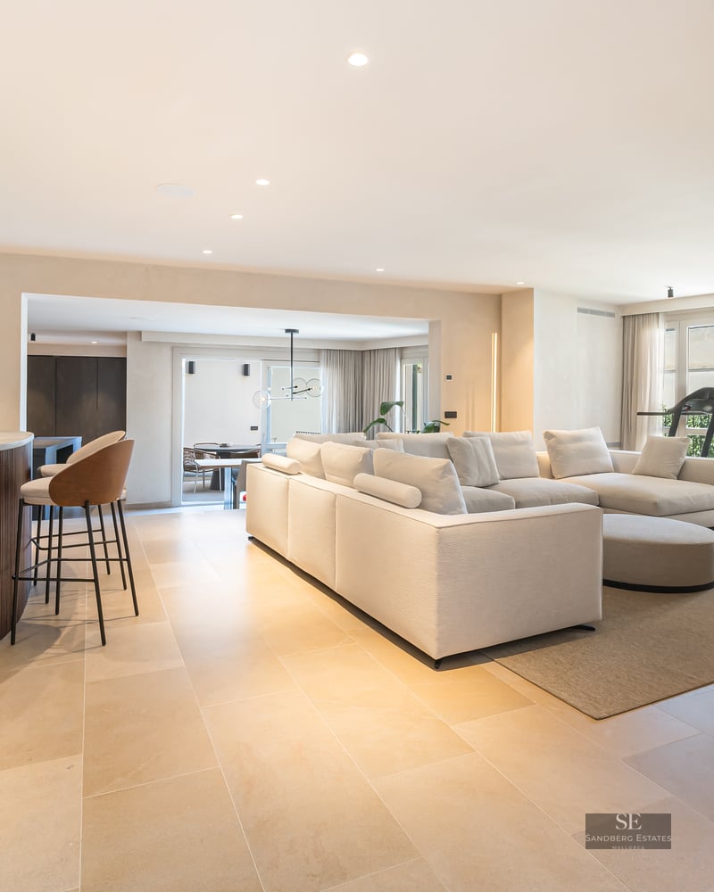 Spacious modern living room with a large white sofa, wooden bar counter, and natural stone flooring.