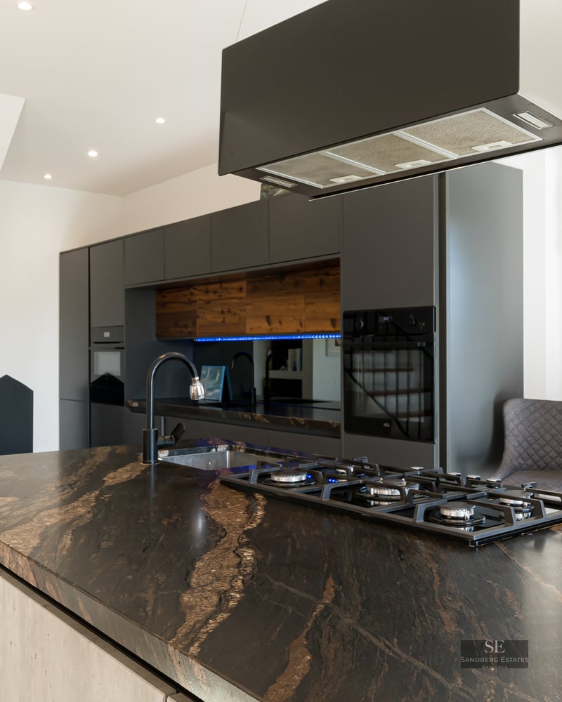 Modern kitchen featuring a large black marble island with a gas stove and a view of mountains through a window.