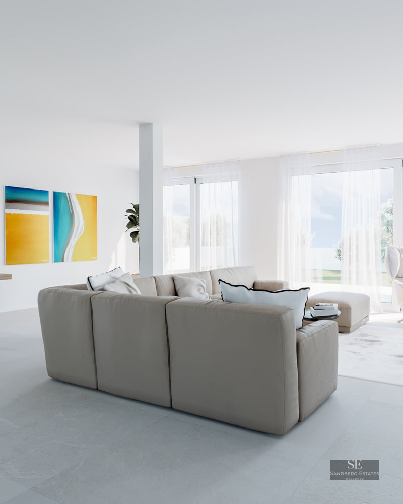 Bright minimalist living room with beige sofa, blue dining chairs, and large windows overlooking a garden.