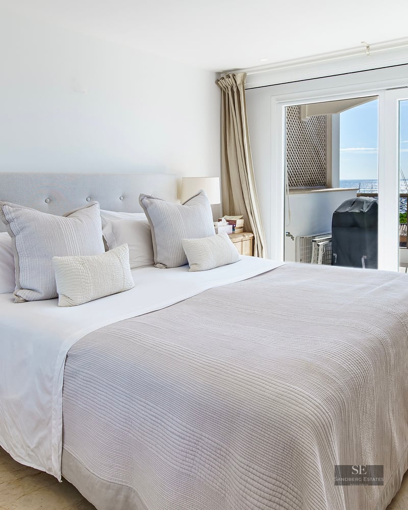 Bright bedroom featuring a large bed, wooden nightstands, and sliding glass doors with views of the sea and marina.