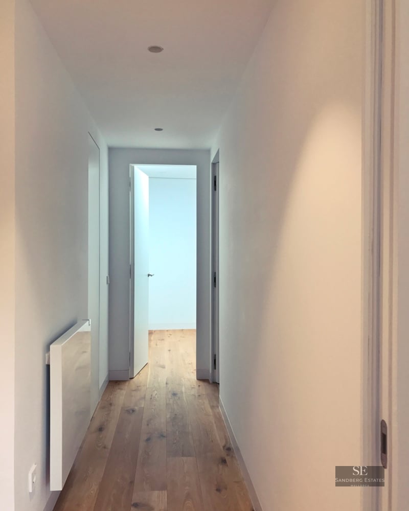 Narrow white hallway with light oak wood floors and minimalist white doors.